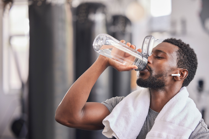 Water bottle, tired black man in gym and resting after fitness workout, healthy sports exercise and muscle growth training. Rest, motivation and thirsty athlete drinking water for hydration wellness