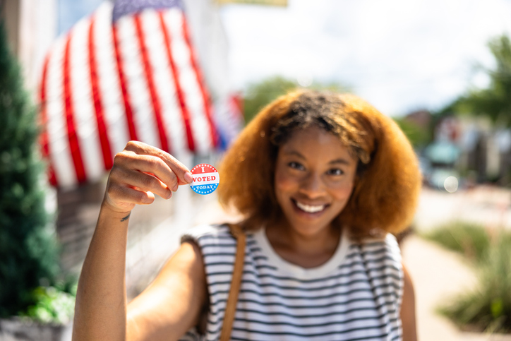 Portrait of a beautiful black woman in front of an American Flag with I Voted sticker